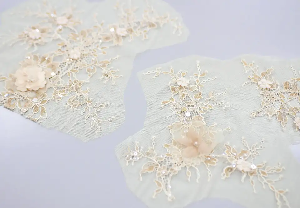 淡い色の生地に、スパンコールや花の立体的な刺繍が華やかに施されたレース生地
