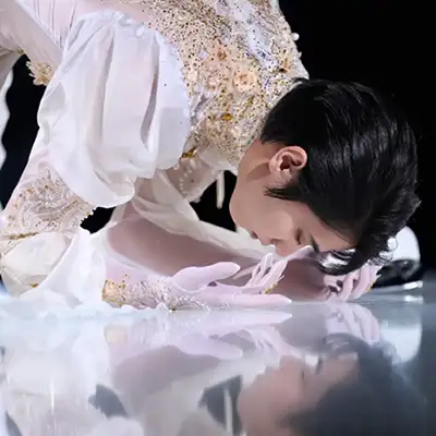写真集『Couture on Ice 羽生結弦×伊藤聡美』より、白とゴールドの装飾が施された衣装を着て氷上に深く身をかがめる羽生結弦の写真