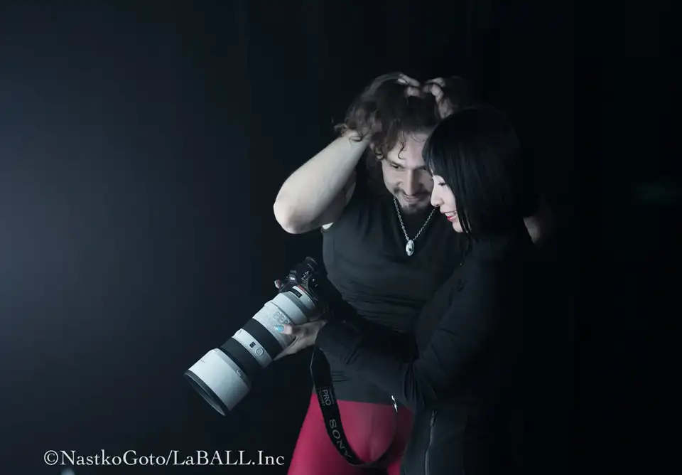 大きな白い望遠レンズが付いたカメラを、一緒に笑顔で覗き込むイワン・ワシリーエフと写真家の後藤奈津子。